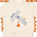 Cream t-shirt with "You Say Soccer, I Say Football" graphic and traffic cone.
