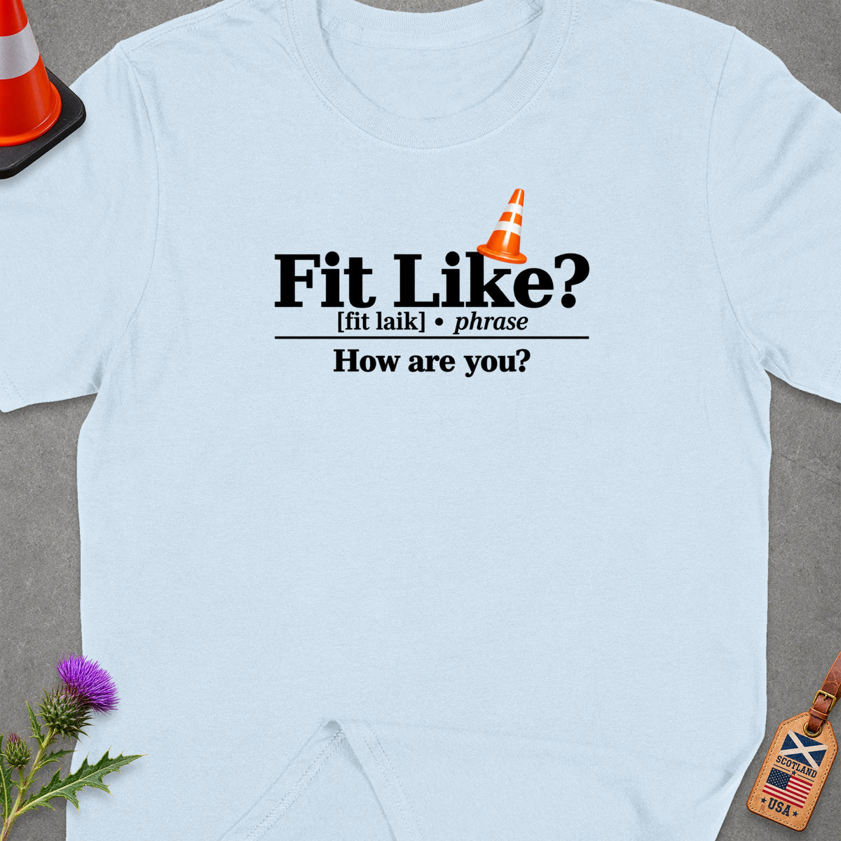 Light blue t-shirt with "Fit Like? [fit laik] phrase How are you?" text.