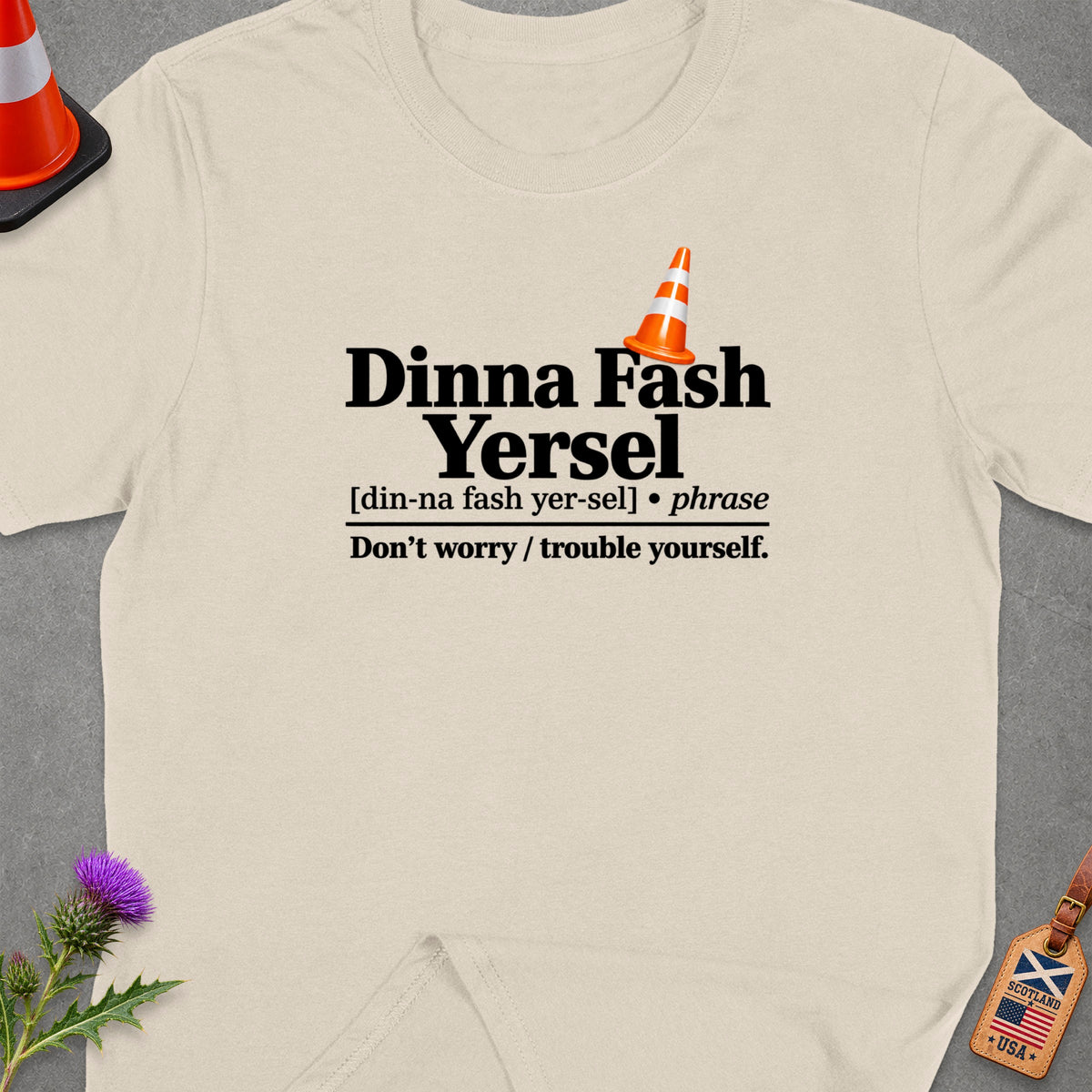 Cream t-shirt with "Dinna Fash Yersel" text and Scottish-American flag tag.