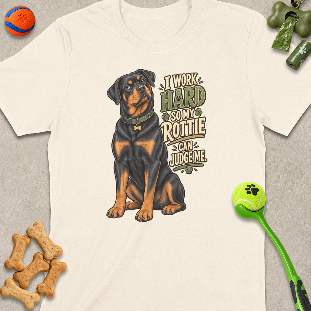 Rottweiler illustration on a cream t-shirt with text "I Work Hard So My Rottie Can Judge Me".