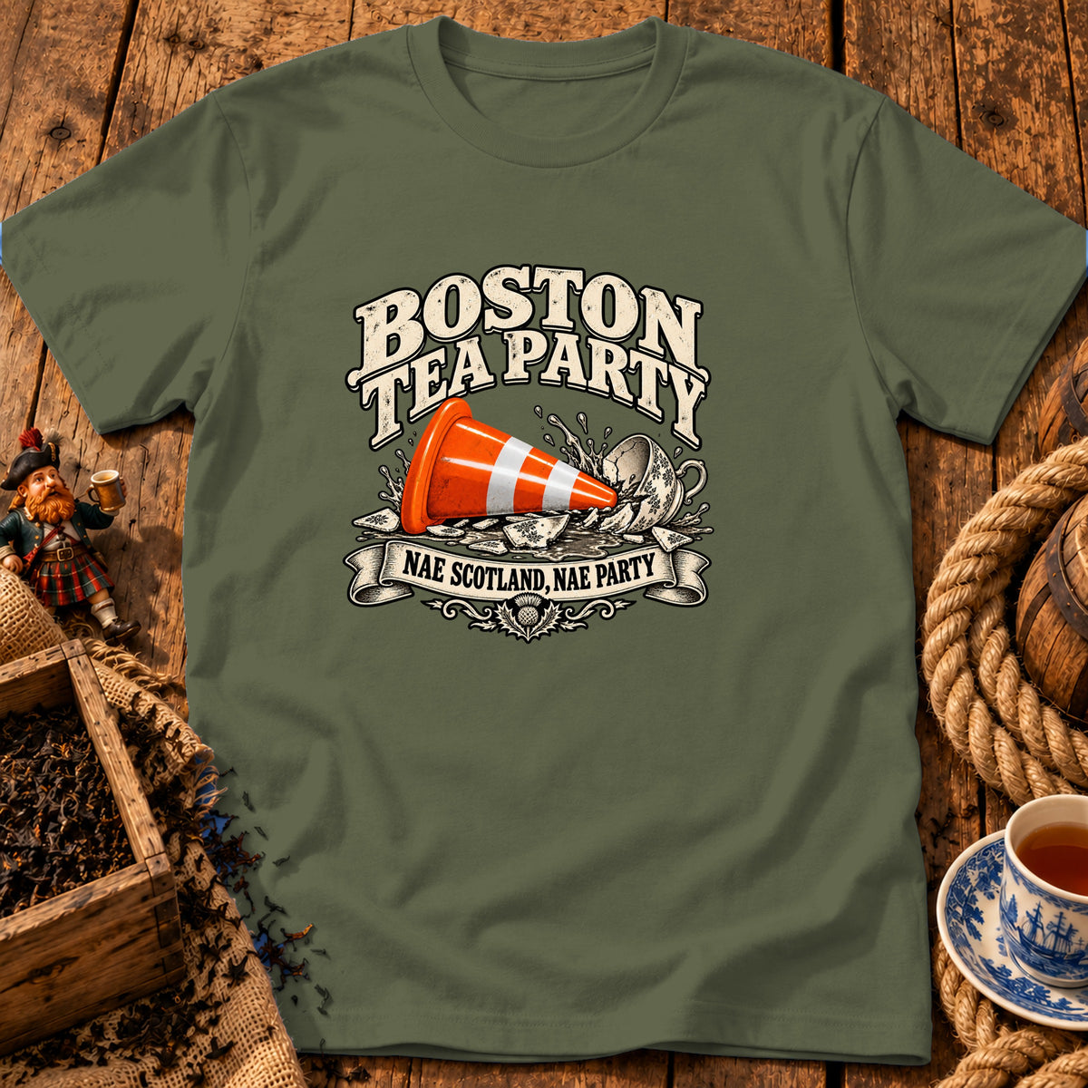 Olive green t-shirt featuring a graphic with a traffic cone in a broken teacup and text reading BOSTON TEA PARTY.