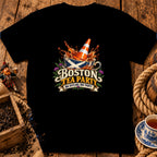A black t-shirt printed with a Scottish-themed Boston Tea Party graphic on a rustic wooden background.