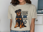 Rottweiler dog illustration with text "SECURITY SYSTEM HAS PAWS" on a cream t-shirt.
