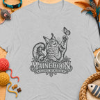 Maine Coon cat playing with butterfly graphic on light gray t-shirt.