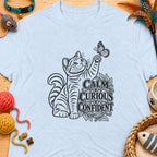 Light blue t-shirt with a tabby cat reaching for a butterfly and text "CALM CURIOUS CONFIDENT".