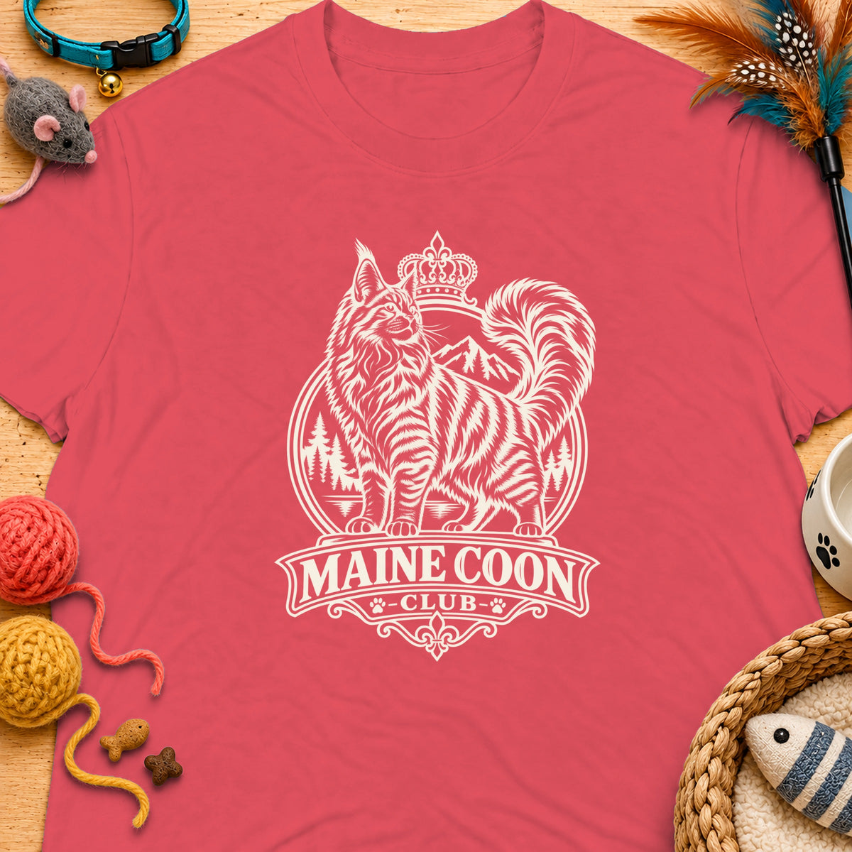 Maine Coon Club emblem featuring a regal cat with mountains and crown, on a pink t-shirt.