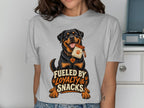 Rottweiler wearing a dog tag and holding a snack bag on a t-shirt with text.