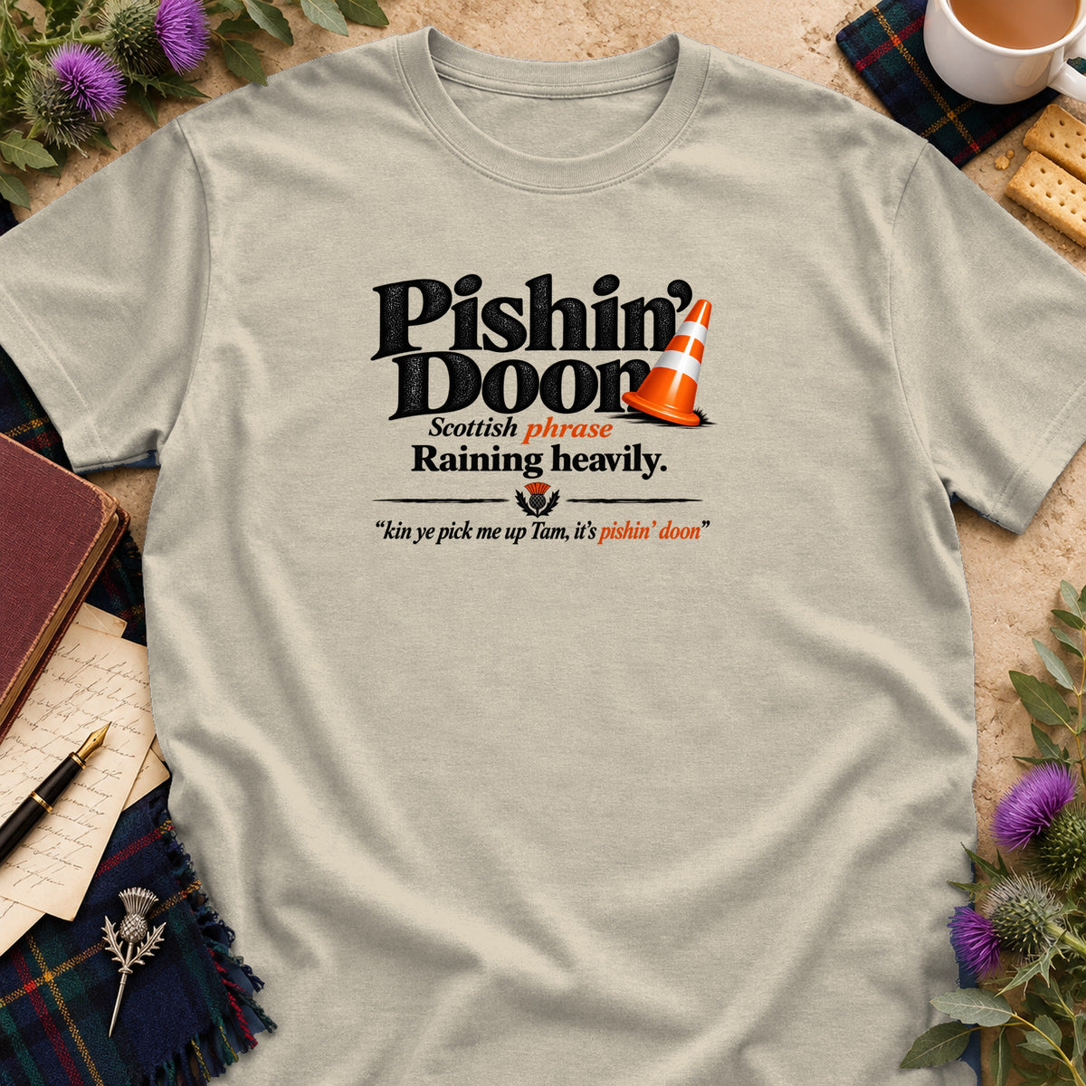 A beige t-shirt printed with the Scottish phrase Pishin Doon, translating to raining heavily.