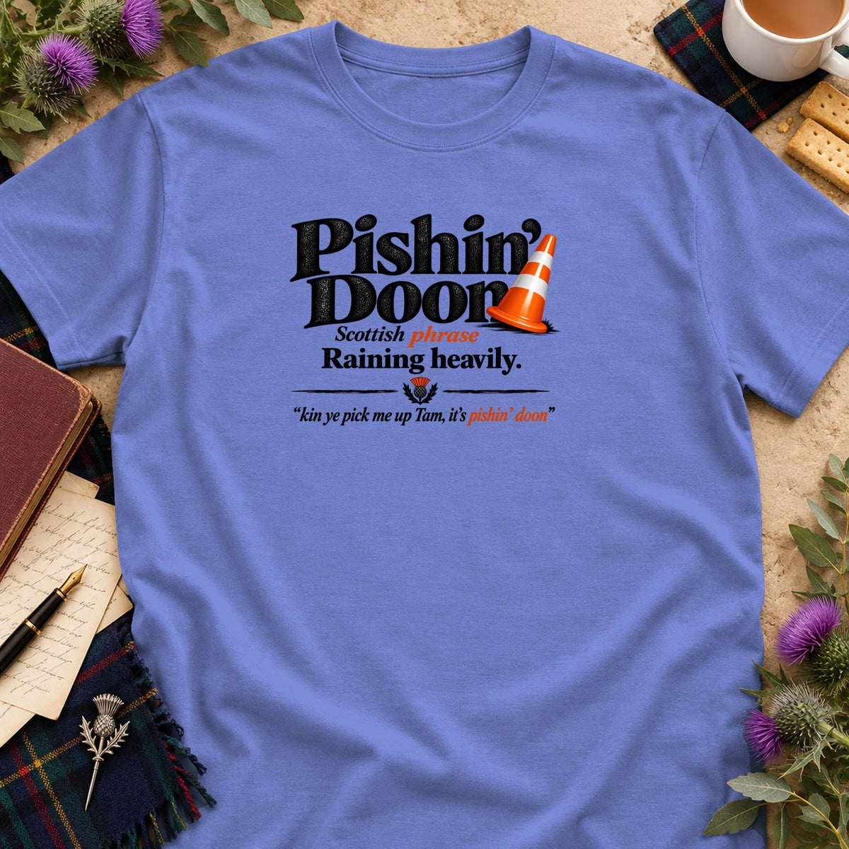 Periwinkle t-shirt with black text reading Pishin Doon, Scottish phrase meaning raining heavily, with an orange traffic cone.