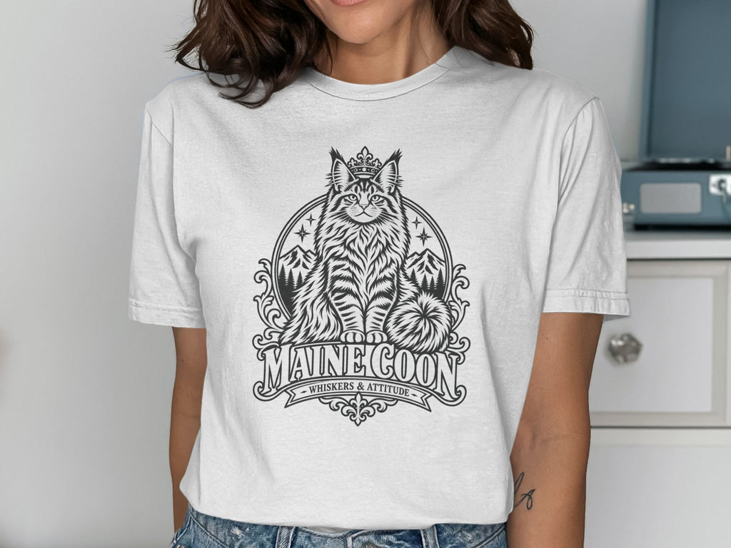 White t-shirt with black graphic of a crowned Maine Coon cat and text "MAINE COON WHISKERS & ATTITUDE".
