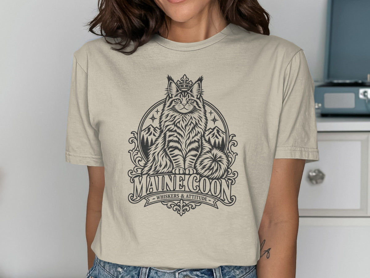 T-shirt with graphic of crowned Maine Coon cat, mountains, and text "MAINE COON WHISKERS & ATTITUDE".
