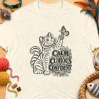 T-shirt with a black line drawing of a cat reaching for a butterfly, text reads "Calm Curious Confident".