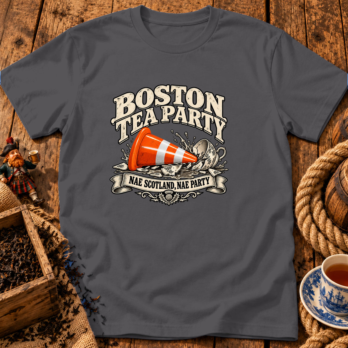Dark grey t-shirt featuring a graphic with an orange traffic cone inside a smashed teacup and text reading BOSTON TEA PARTY and NAE SCOTLAND, NAE PARTY.