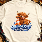 Fluffy Highland cow with a traffic cone and text "One Fur the Road? Nae Chance."