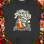 T-shirt featuring a hedgehog wearing a Santa hat holding an orange traffic cone with "Wee Prickly" text.