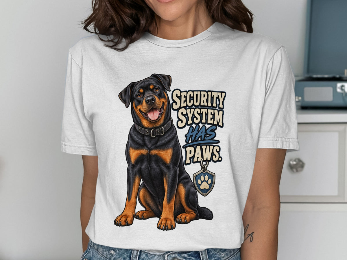 White t-shirt with a Rottweiler illustration and text "SECURITY SYSTEM HAS PAWS."