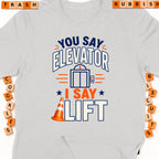Gray t-shirt with text "You say Elevator, I say Lift" and an elevator graphic.