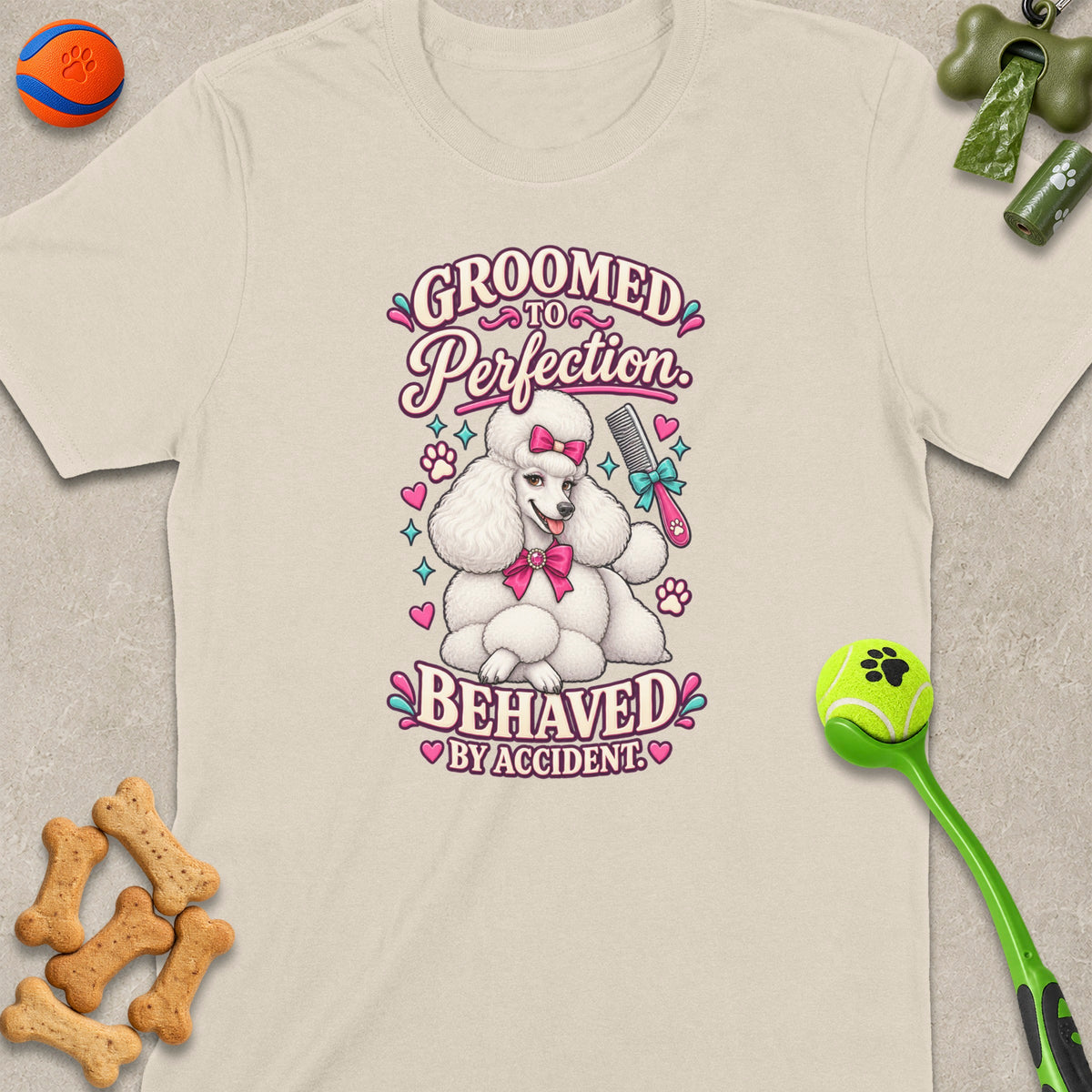 White poodle graphic on a cream t-shirt with text "Groomed to Perfection Behaved by Accident."