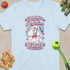 Light blue t-shirt with illustration of a white poodle holding a comb and text: "GROOMED TO PERFECTION BEHAVED BY ACCIDENT."